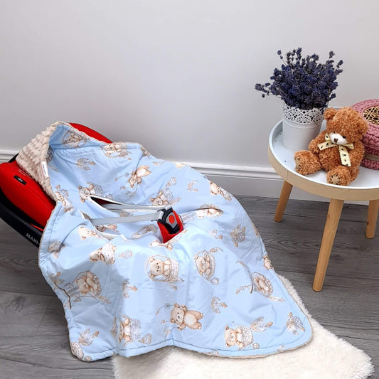 A light blue baby car seat cover with a teddy bear pattern, draped over a red baby car seat on a white rug in a styled room corner with a side table and teddy bear.