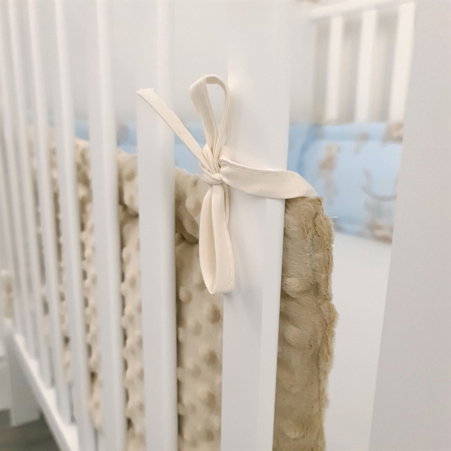 Close-up of a crib with beige textured bumper and cream bow