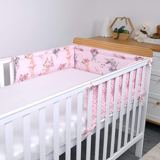White crib with pink floral crib bumper in a room with wooden dresser and toys.