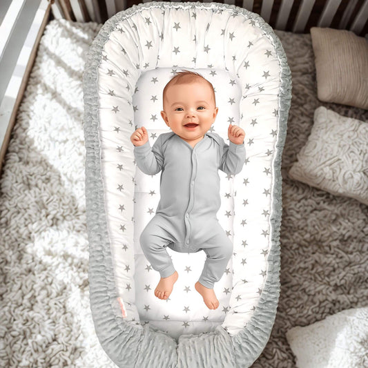 Baby in a star-patterned sleeping pod crib inside a larger gray crib with white bedding.