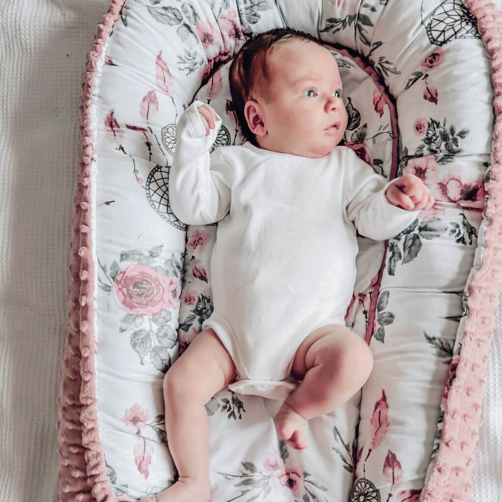 newborn baby girl in the baby nest in pink and floral pattern from evcushy baby sleep essentials