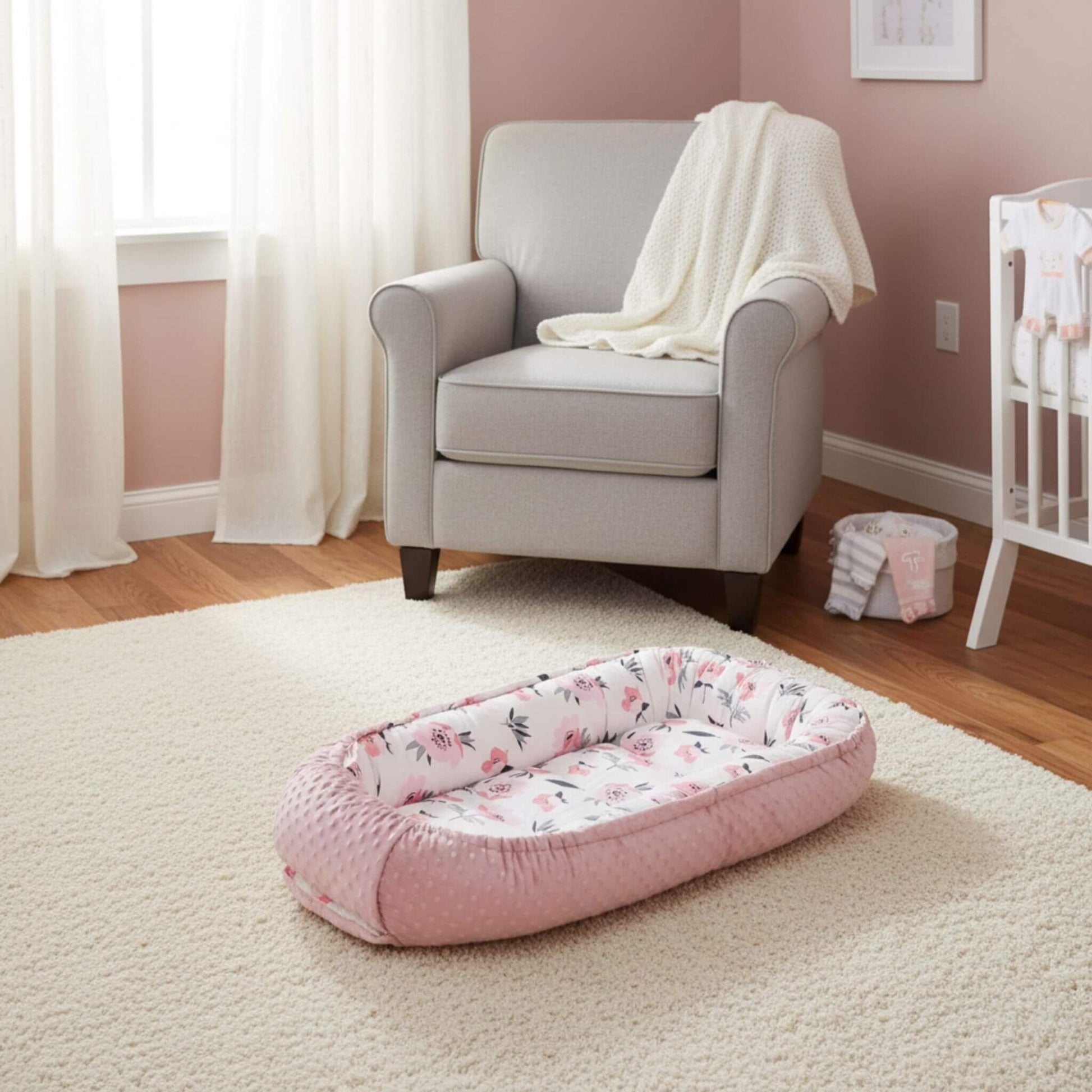 Pink floral baby bassinet in a nursery with a chair and crib.