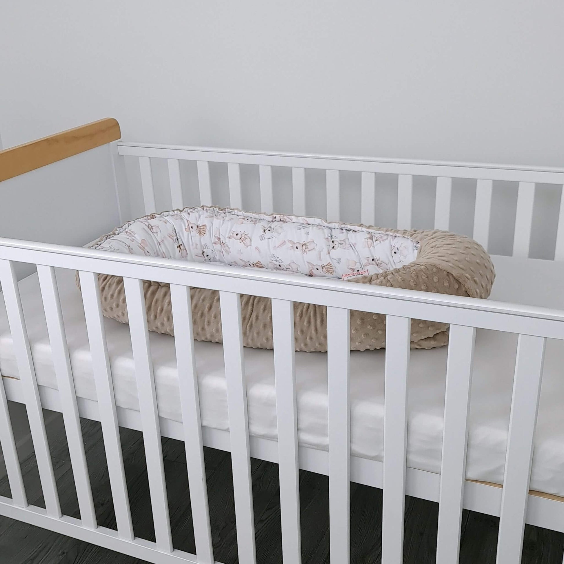 White crib with a beige bassinet inside against a plain wall