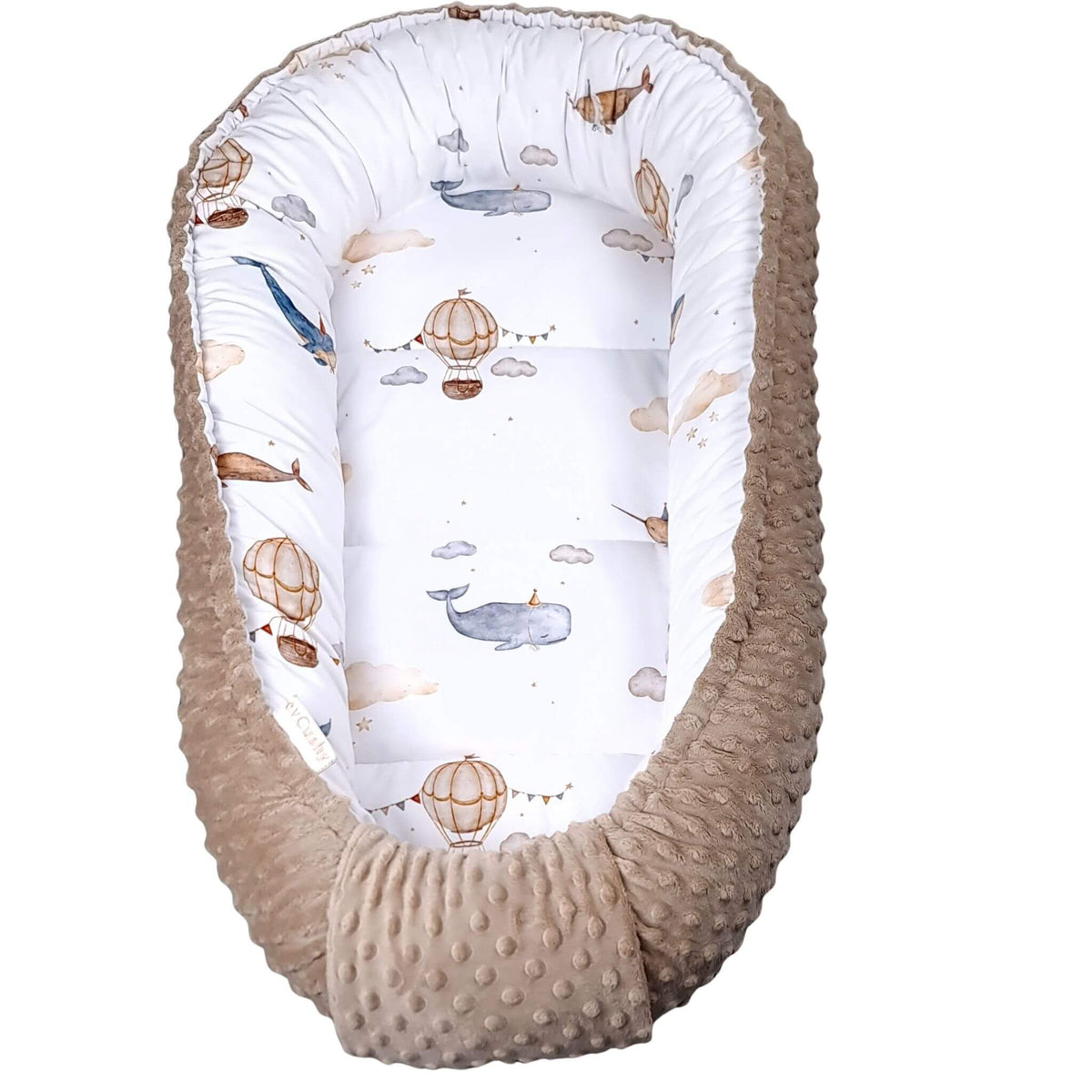 A baby Moses basket bassinet with a textured beige minky dot fabric exterior and a white interior printed with whimsical whale and hot air balloon illustrations.