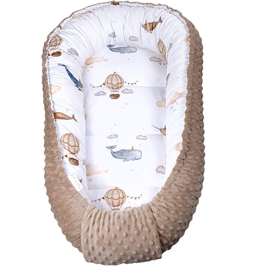 A baby Moses basket bassinet with a textured beige minky dot fabric exterior and a white interior printed with whimsical whale and hot air balloon illustrations.