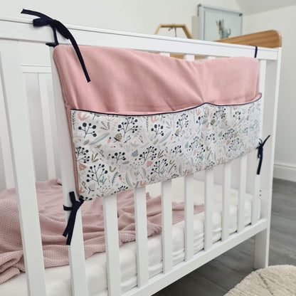 White crib with pink and floral bumper pad in a nursery setting organizer for baby essentials