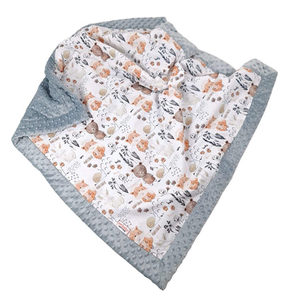 A baby blanket with a textured light gray minky dot border and a white printed inner side featuring teddy bears, trees, and flowers in soft orange, brown, and gray tones, shown on a plain white background.