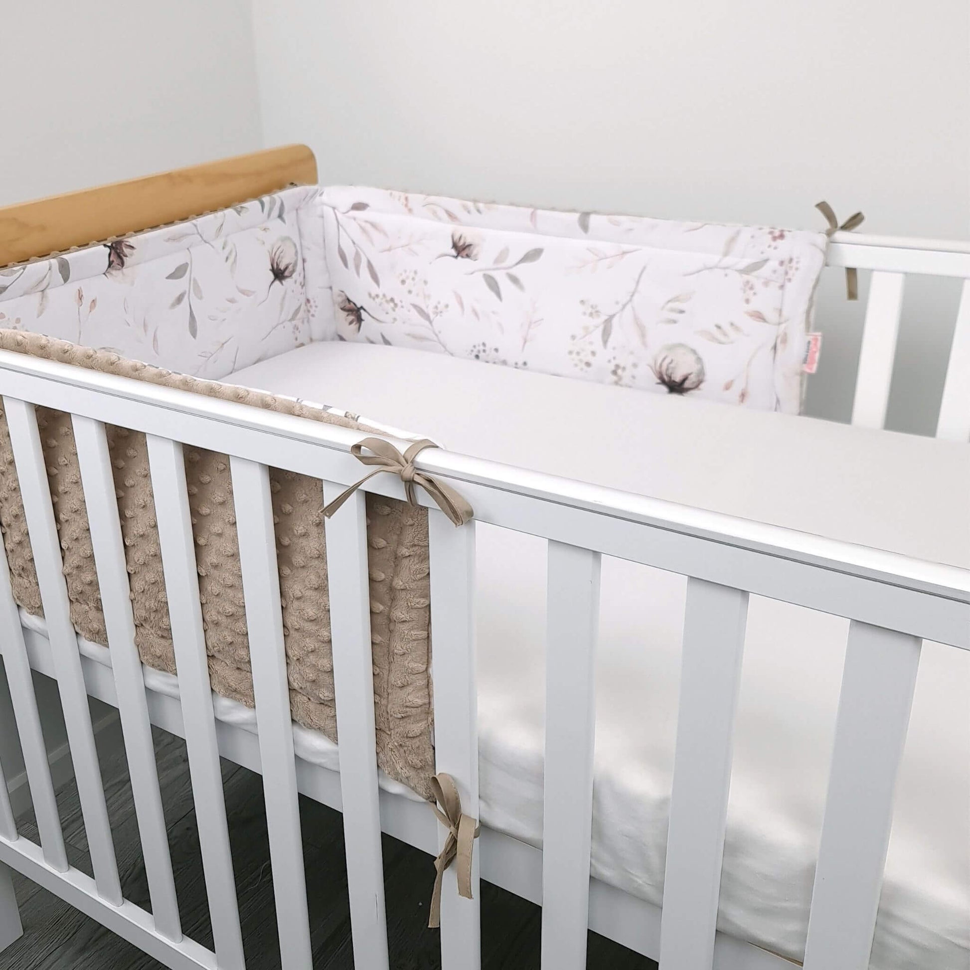 White crib with floral bumper pad  in a neutral room.