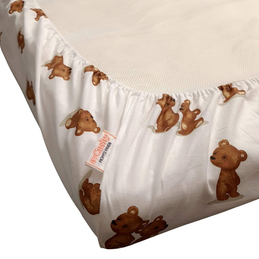 A close-up of a white fitted crib sheet mattress cover with an allover print of brown teddy bears, shown on a mattress corner. A fabric tag reading evcushy is visible