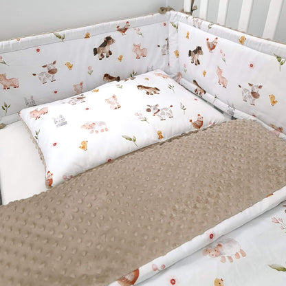 A baby crib bedding set featuring a white bumper pad and pillow with a whimsical animal print, paired with a textured taupe-brown minky dot blanket.