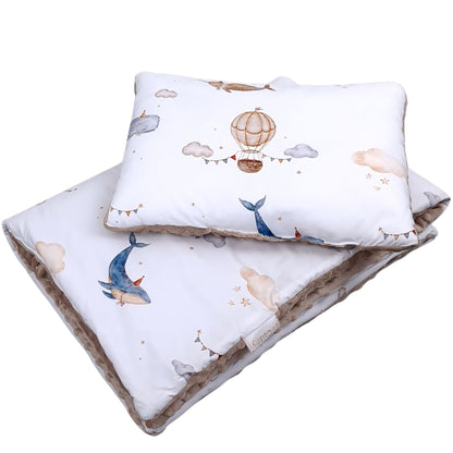 Close-up of cotton fabric baby bedding set featuring whales, clouds and hot air balloons in soft neutral tones
