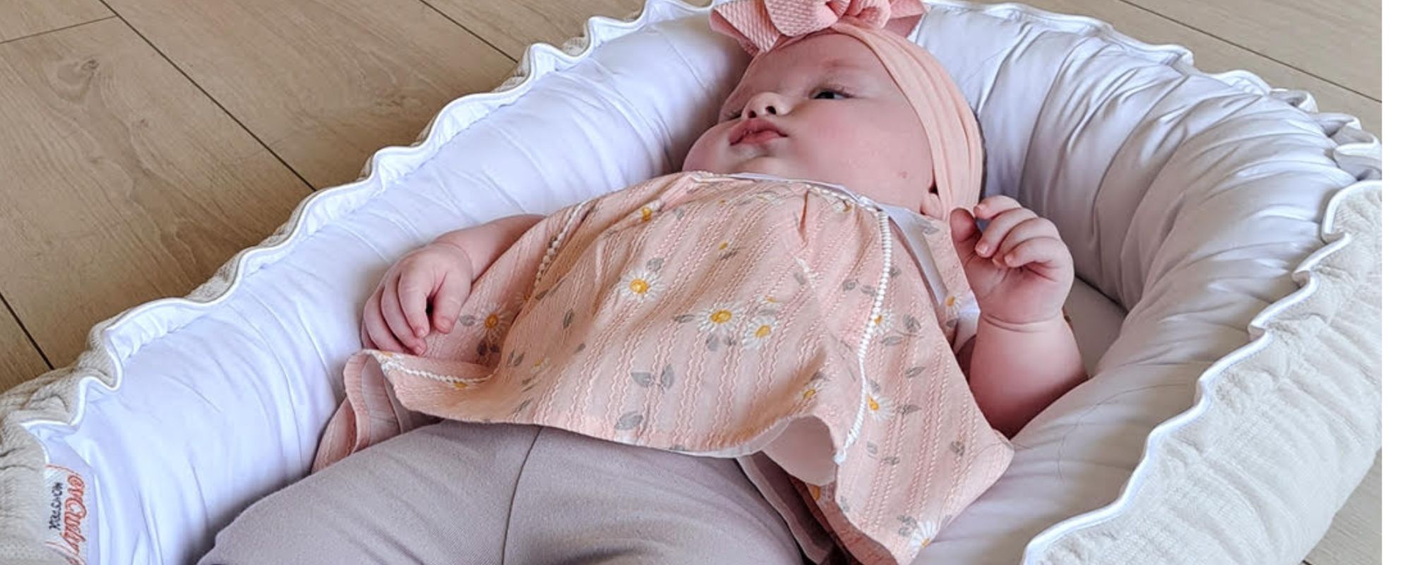 Baby in a pink outfit and hat lying in the white and beige nest from evcushy