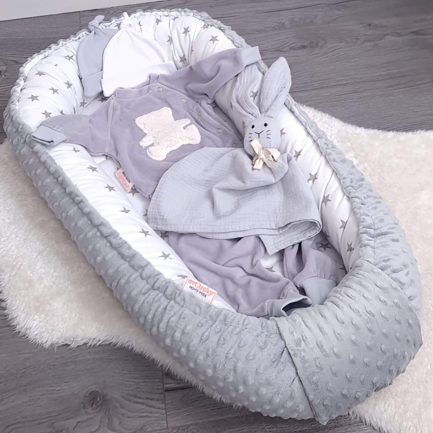 Grey stars baby nest styled with cotton bunny comforter and newborn clothes – soft baby bedding and nursery essentials by Evcushy