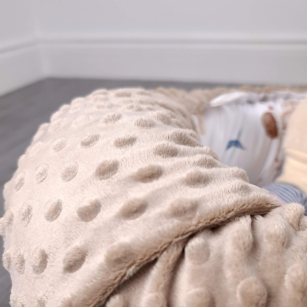A close-up of a soft beige baby nest fabric with a hot air balloons pattern, draped over a baby's body in a bedroom setting.